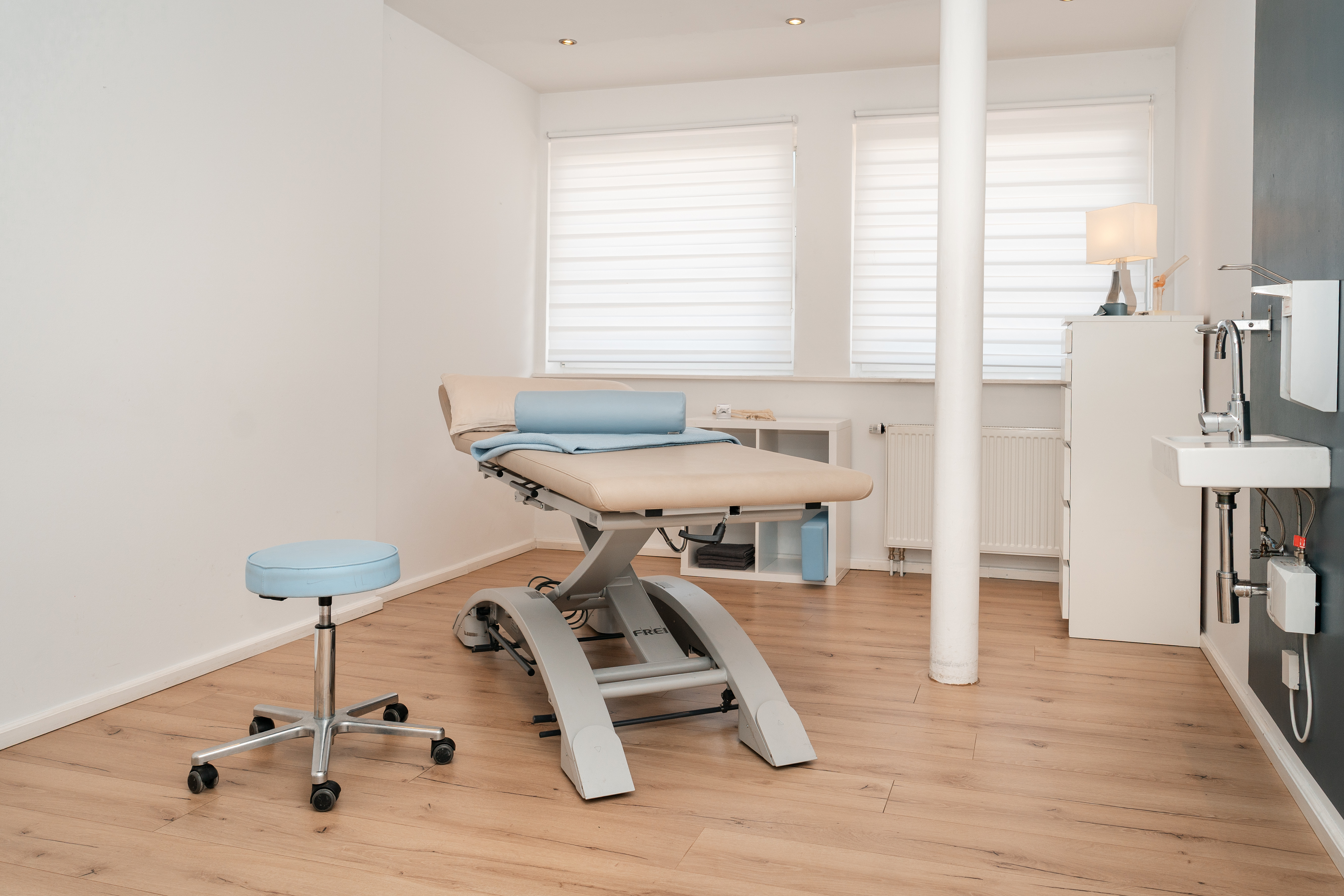 Heller Behandlungsraum mit Therapieliege und großen Fenstern